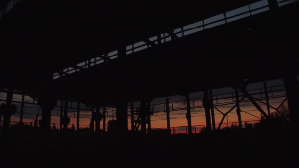 Grande armazém abandonado ou oficina de fábrica com silhuetas de muitas estruturas metálicas ao pôr do sol — Vídeo de Stock