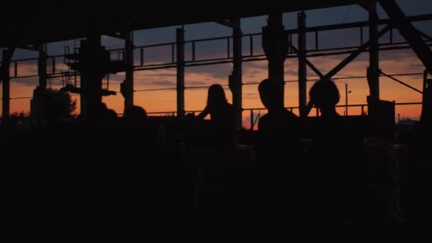 Minsk, Biélorussie, 9 janvier 2022 : Silhouettes d'un groupe de personnes qui jouent dans un hangar abandonné avec des structures métalliques au coucher du soleil — Video