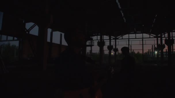 Mińsk, Białoruś, 9 stycznia 2022: Sylwetka człowieka z gitarą i śpiewem z przyjaciółmi w starym budynku magazynu o zachodzie słońca — Wideo stockowe