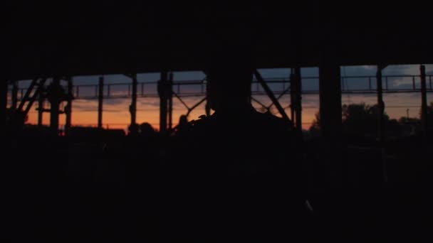 Minszk, Fehéroroszország, 2022. január 9: Silhouette of a man with a guitar singing with others in a abandoned factory workshop at sunset — Stock videók