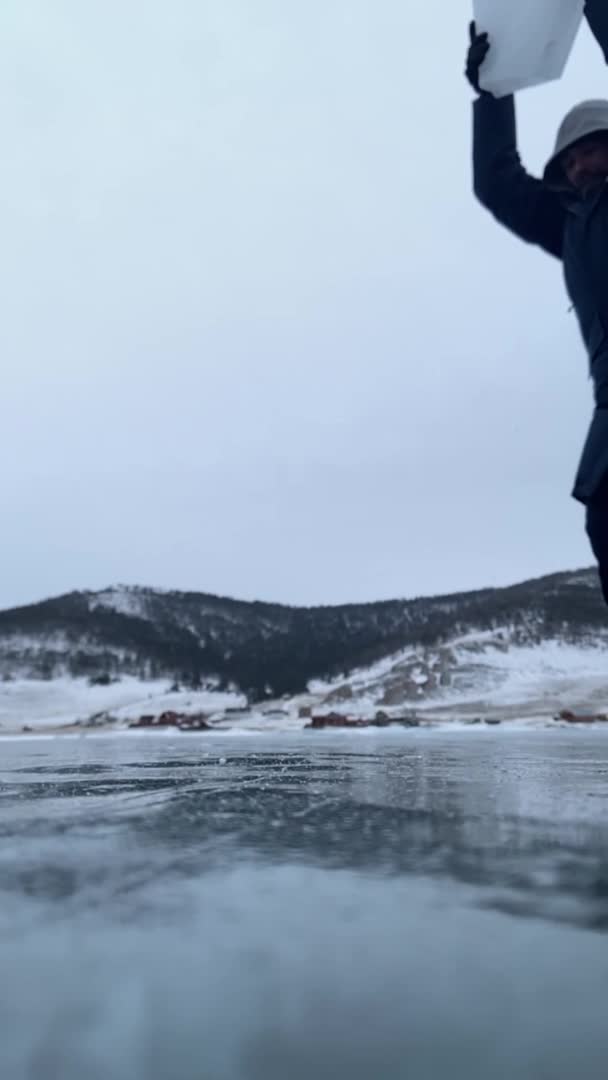 Een bebaarde jongeman breekt een stuk ijs op het oppervlak van het Baikalmeer en kleine transparante stukjes vliegen in de cameralens. Verticale video. Langzame beweging — Stockvideo