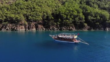 Türkiye, Kemer - 20 Ekim 2021: Koyun mavi sularında turistlerle yatların ve güneşli bir yaz gününde ağaçlarla kaplanmış kayalık adaların insansız hava araçlarıyla vurulması