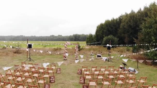 Vista aérea de un área abierta decorada para la ceremonia de boda con filas de sillas y un arco de flores — Vídeo de stock