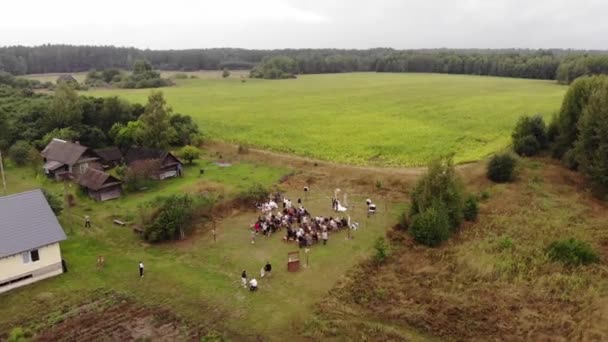 Mińsk, Białoruś - 29 czerwca 2021 r.: Strzelanie z drona ceremonii ślubnej z wieloma gośćmi na polanie w pobliżu domów na wsi — Wideo stockowe