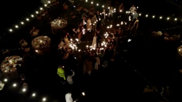 2021年6月29日，白俄罗斯明斯克：在一个装饰着燃烧的花环和蜡烛的空地上，新婚夫妇被一群闪烁着火花的客人围住跳舞的空中景象 — 图库视频影像