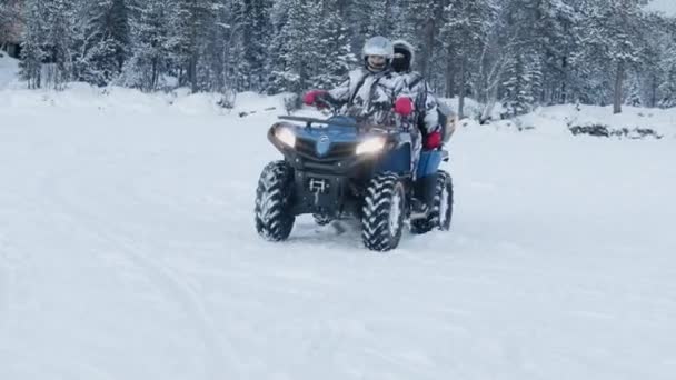 Murmansk region, Rusko - 10. ledna 2021: Pár v helmách a speciálních oblecích jezdí v zimě na ATV na lesní cestě. Zpomalený pohyb — Stock video