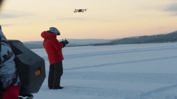 Región de Murmansk, Rusia - 10 de enero de 2021: Un hombre se para en un campo cubierto de nieve y usa un control remoto para comandar un dron. Movimiento lento — Vídeo de stock