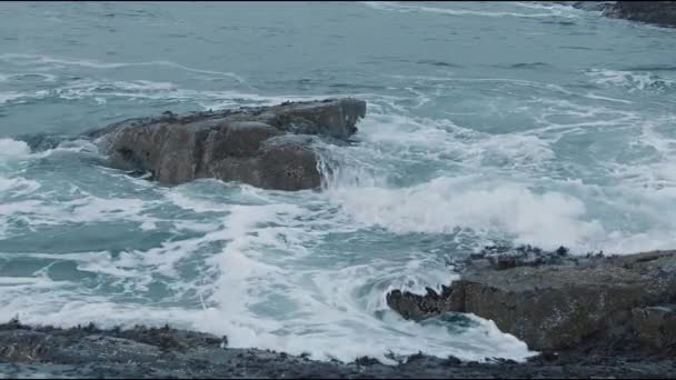 Deniz dalgaları kayalık bir sahilde yuvarlanır ve su büyük kayaların üzerinden taşar. Yavaş çekim — Stok video