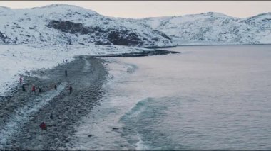Karlı dağları olan güzel bir deniz manzarası ve kumsaldaki ejderha yumurtalarında bir grup turist. Yavaş çekim