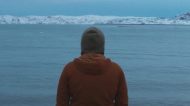 Genç bir adam kıyıda duruyor ve uzaklığa bakıyor. Yansıma konsepti. Yavaş çekim