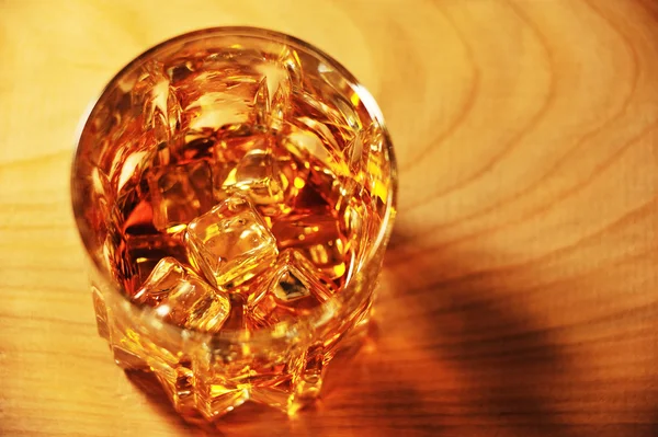 Glass of whisky with ice against yellow background — Stock Photo, Image