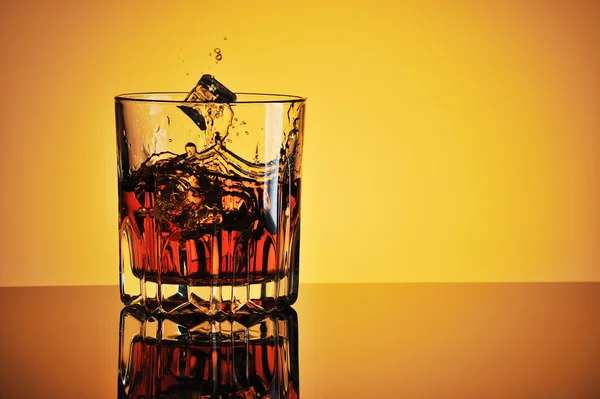 Glas whisky met ijs tegen gele achtergrond Stockafbeelding