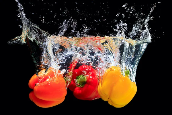 Red, orange and yellow peppers splashing water — Stockfoto