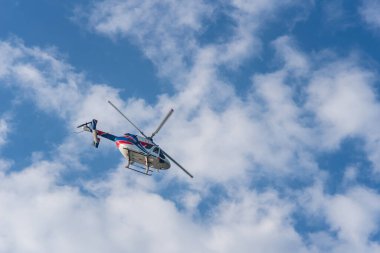 Beyaz bulutlu mavi gökyüzünün arka planında bir helikopter..