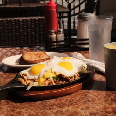 Sosis ve yumurta kahvaltı tavası, kızarmış ekmek ve portakal suyu.