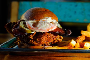 Baharatlı çıtır tavuklu sandviç, patates kızartması ve domuz pastırması.