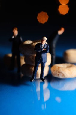 Miniature businessmen inspect toasted oat loop cereal for quality control