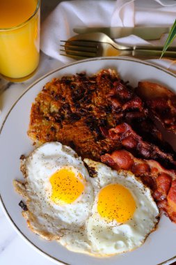 American breakfast two eggs sunny side up with bacon hash browns and a glass of fresh squeezed orange juice