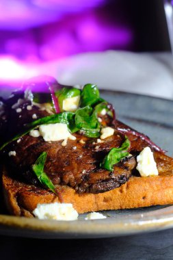 Open faced portobello mushroom sandwich on toast with feta cheese and garnished with sauteed chard