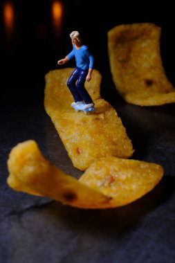 Skateboarding miniature man rides on junk food corn chip 