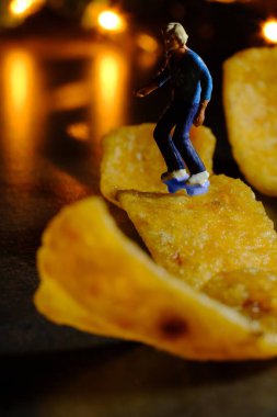 Skateboarding miniature man rides on junk food corn chip 