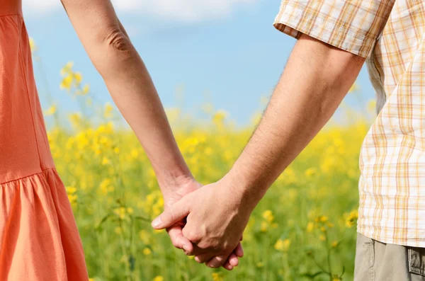 Casal de mãos segurando apertado em um belo campo amarelo — Fotografia de Stock