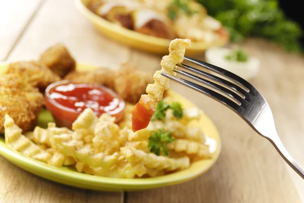 Batatas fritas e frango no prato na mesa de madeira — Fotografia de Stock