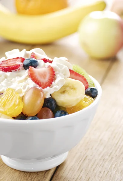 Sweet tasty fruit salad in the bowl with whipped cream — Stock Photo, Image