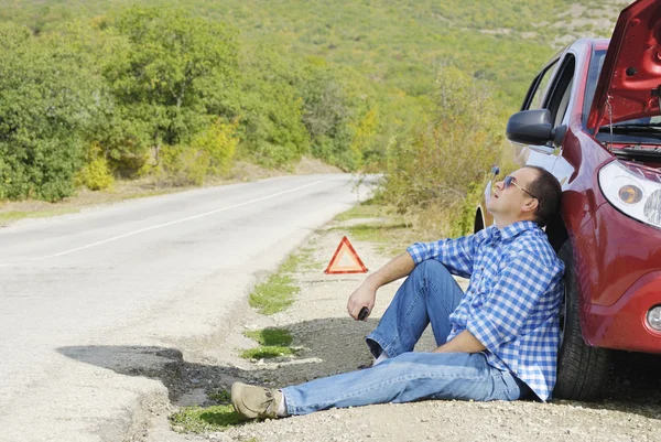 成人男性は彼の壊れた車の近くに座っています。 — ストック写真