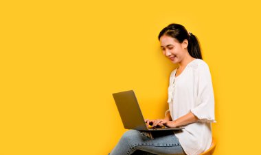 Dizüstü bilgisayarında çalışan Asyalı bir kadın ve mutlu bir gülümseme stüdyoda sarı bir arka planda mutlu bir çalışma konsepti.