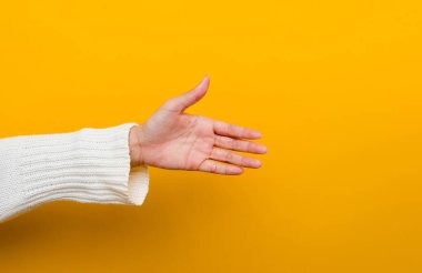 hand of a young woman wearing a white long sleeve prom dress on a yellow background in a photo studio