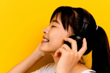 Müzik dinleyen beyaz elbiseli genç bir Asyalı kadın mutlu bir şekilde gülümsüyor. Mutlu insanlar yaşam tarzı konsepti kopyalama alanı modeli kulaklıkla müzik dinlemek