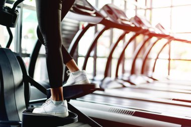Spor salonundaki Asyalı kız otomatik koşu bandında egzersiz yapıyor.