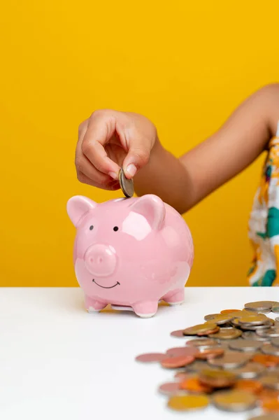 Saving money Young girl's hand balances coins in a piggy bank, pink pig, planting a savings plan for children, money saving concept.