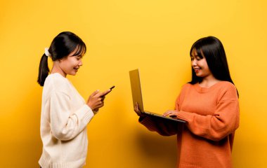 Two Asian women working on laptop and phone. at the same time Two of them were communicating online and showing happy smiles.