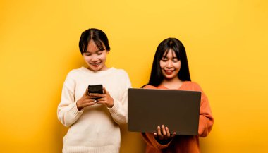 Two Asian women working on laptop and phone. at the same time Two of them were communicating online and showing happy smiles.