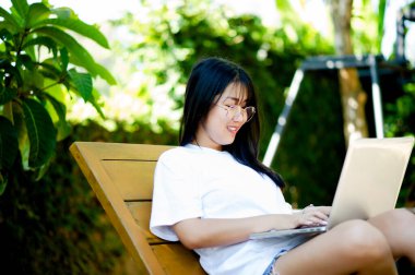 Ofisin dışında, evinde, parkta çalışırken bilgisayarında çalışırken gülümseyen neşeli Asyalı bir kadınla çalışmaktan mutluluk duyarım. Tatilde evde çalışmak ve online çalışmak