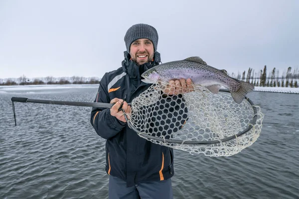 Glad Fiskare Med Regnbågsfisk Och Landningsnät Vinterfiske Vid Snöig Sjö — Stockfoto