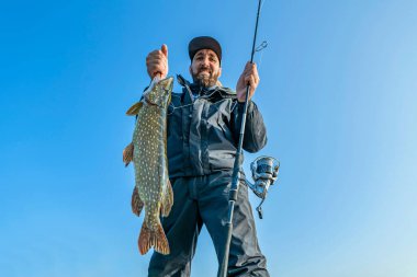 Success pike fishing. Happy fisherman with big fish trophy and spinning rod tackle clipart