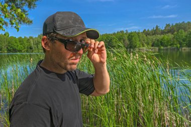 Şüpheci bir bakış. Şapkalı adam, güneş gözlüğü altında, aşağılayıcı, şüpheci ve kuşkucu bir şekilde dışarıyı izliyor.