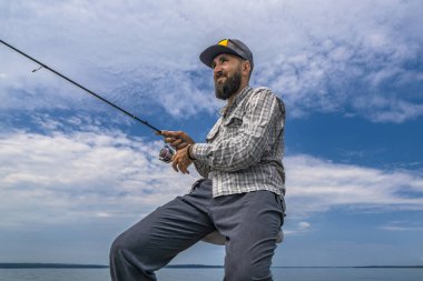 Spinning fishing. Fisherman wait fish strike bite. Bearded angler with rod on blue cloudy sky background