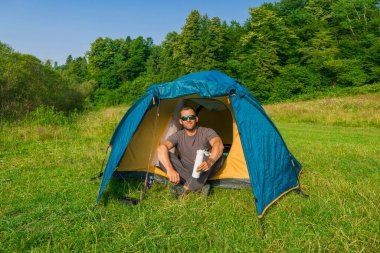 Açık havada dinleniyor. Termoslu bronzlaşmış bir adam kamp çadırında oturup dinleniyor ve balık tutuyor.