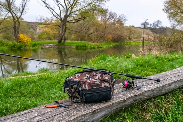 釣り合いセット 小さな川の近くの木の丸太の上にリールとペンチ付きの特別な釣竿 回転棒 — ストック写真