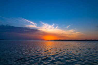 Colorful sunset over lake. Sun hiding behind water horizon. Relaxation landscape