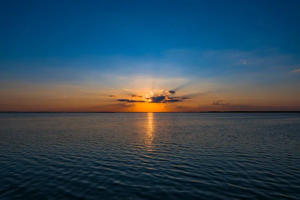湖の上にカラフルな夕日 太陽が水の地平線の後ろに隠れて 赤い日の出と青い曇りの空 リラクゼーションの風景 — ストック写真