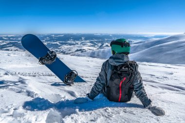 Snowboard sporcusu dağın tepesinde rahatlıyor. Kış serbest kayak sporu