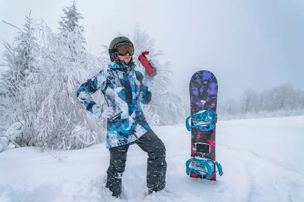 Snowboarder woman with thermos at winter snowy mountains