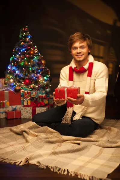 Young smiling man holding red christmas gift — Stock Photo, Image