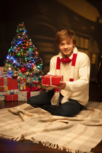 Young smiling man holding red christmas gift — Stock Photo, Image