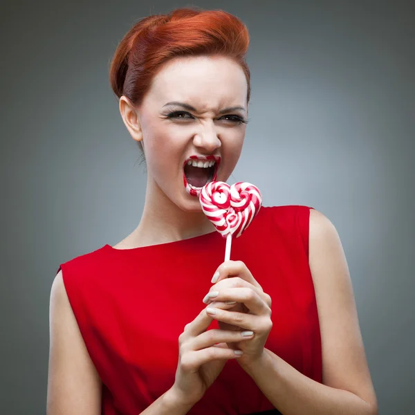 滑稽红年轻漂亮的女人咬棒棒糖 — 图库照片
